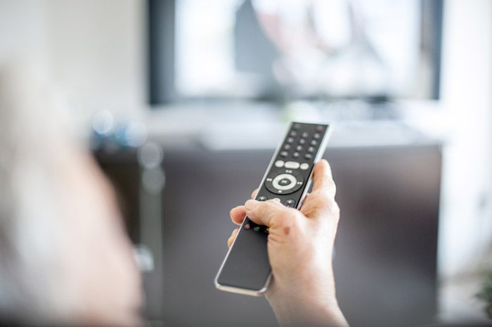 A person pointing a TV remote at the TV
