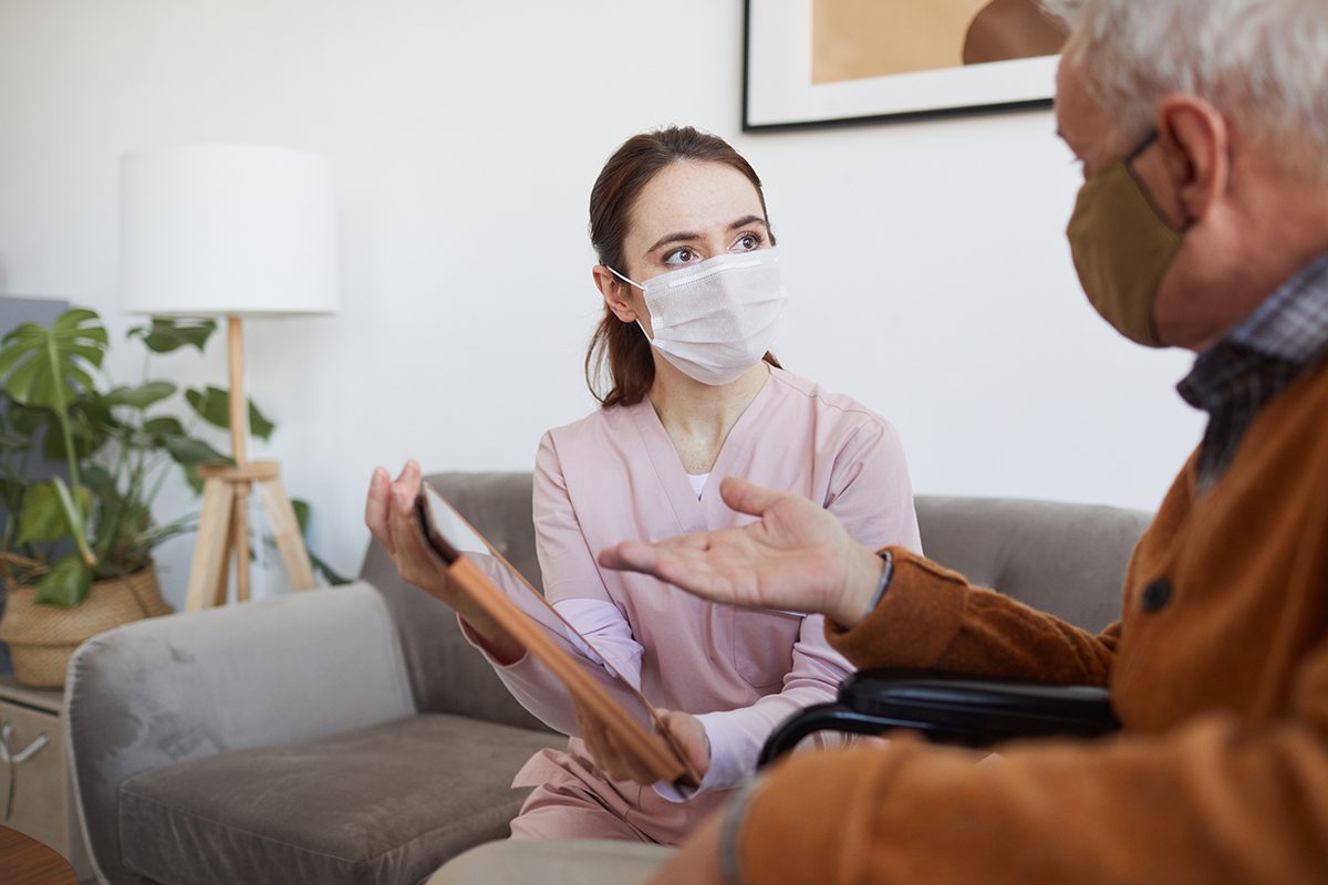 two people wearing masks, sitting and discussing something on a clipboard