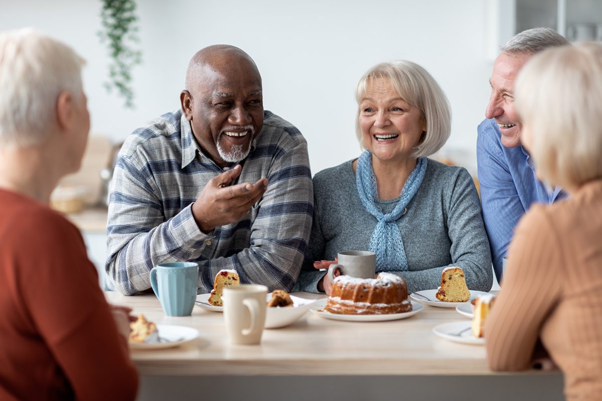 A group of older adults sit together and enjoy a tea cake.